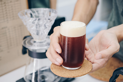 Barista holding and serving a drinking glass of cold brew dip coffee.