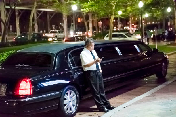 motorista de limusine em pé pelo passeio de carro olhando para o telefone móvel smartphone no bairro de georgetown durante a noite de diversão nocturna de noite escura - 4824 - fotografias e filmes do acervo