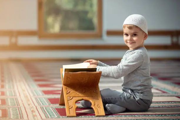 Photo of The Muslim child prays in the mosque, the little boy prays to God, Peace and love in the holy month of Ramadan.