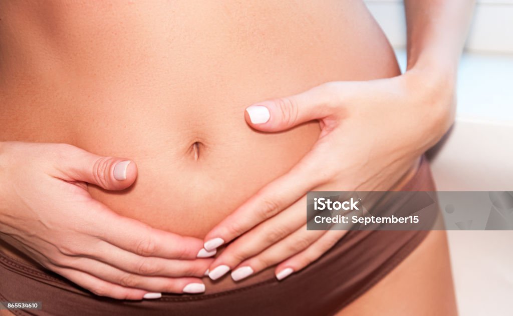 A tanned girl holds her hands to her stomach. IVF concept, pregnancy, digestion, health of the female reproductive system. A tanned girl holds her hands to her stomach. IVF concept, pregnancy, digestion, health of the female reproductive system Abdomen Stock Photo