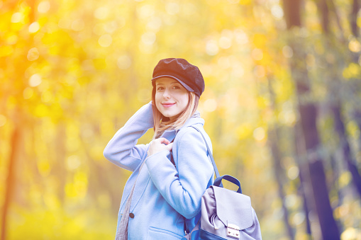 Young redhead woman in blue coat and backpack have a rest in autum park
