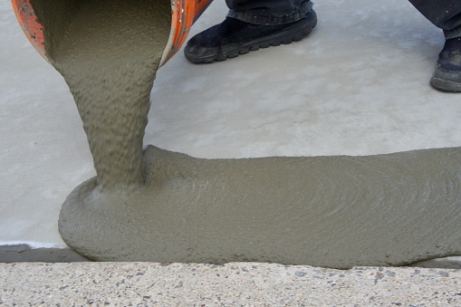 A worker pouring wet cement out of a bucket.