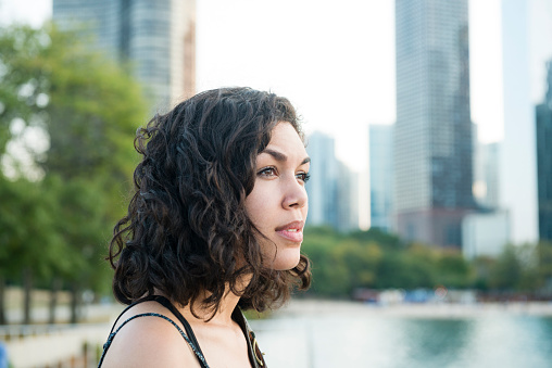 A beautiful, millennial Puerto Rican woman in her 20's stands by Lake Michigan in Chicago, Illinois, a major USA city in the Midwest. She looks out over the water with the famous skyline behind her.