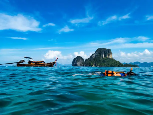 Child snorkeling in Andaman Sea  near Koh Poda with Thailongboat and karst cliff in the background
