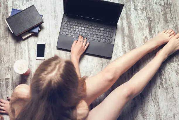 Girl blogger working, prints the text on the laptop, sitting on a floor. Top view