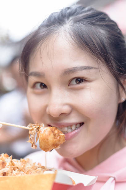 istock woman eating takoyaki with bamboo stick 865585690