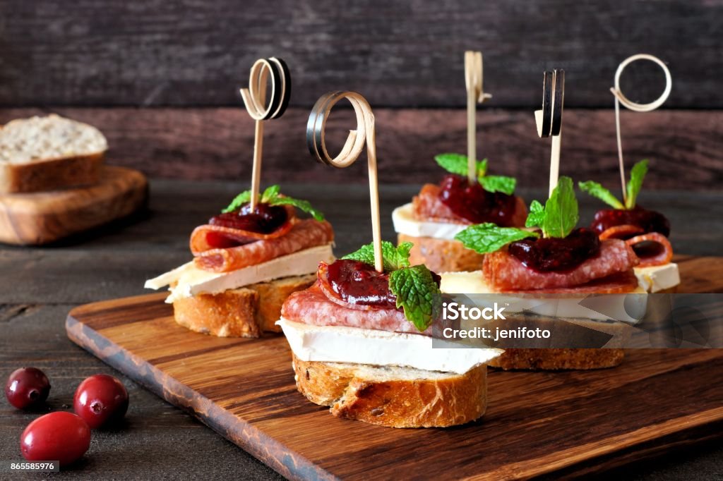Holiday crostini skewers with cranberry sauce Holiday crostini skewers with cranberry sauce, brie, salami, and mint on a wooden server Appetizer Stock Photo