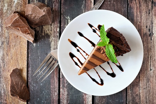 Slice of chocolate cheesecake on plate, above view over a rustic wood background