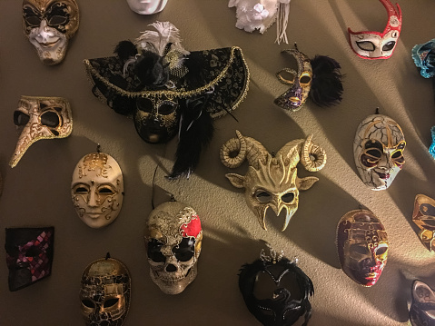 As decorations for a Halloween party at someone's home, this collection of masquerade masks hang on a wall. Some are more traditional of the Venetian masks style, while some are more spooky, intended for Halloween. Shot on an iPhone 6s Plus.