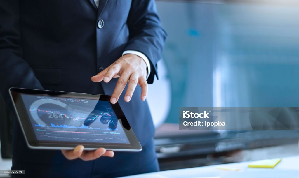 Analyzing data, Businessman working and checking market data in office, hand pointing on the data presented in the chart on tablet Presentation - Speech Stock Photo