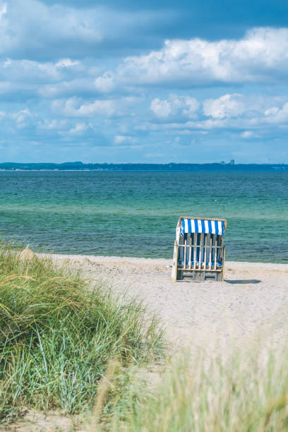 istock Sand dune with grass and blue colored roofed chairs on sandy beach in Background. Travemunde. Germany 865604648