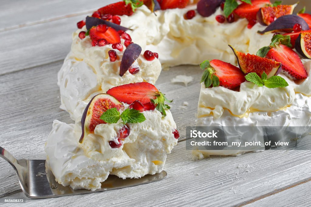 pavlova cake wreath of french meringue pavlova cake wreath of french meringue and whipped cream, decorated with strawberry, figs, pomegranate seeds and mint cut in slices and one piece on cake paddle, close-up Christmas Stock Photo