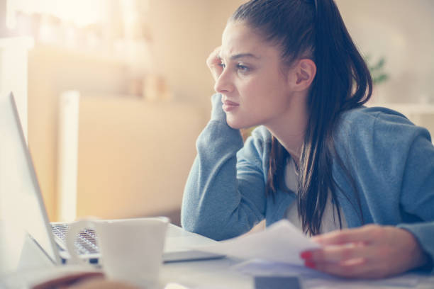 istock Young girl at home holding  bills and using laptop. 865612234