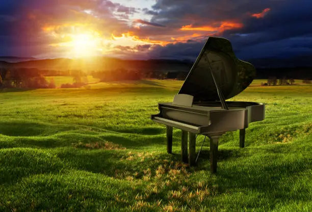 Black glossy piano on the meadow under the dramatic sky with sunny lights. Photos montage with 3D render illustration.