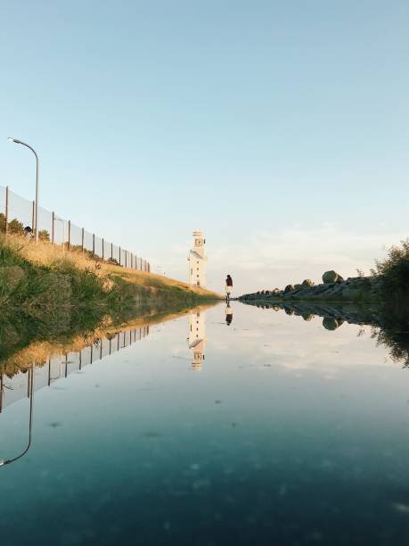 Woman Standing by Lighthouse Reflected in Big Puddle