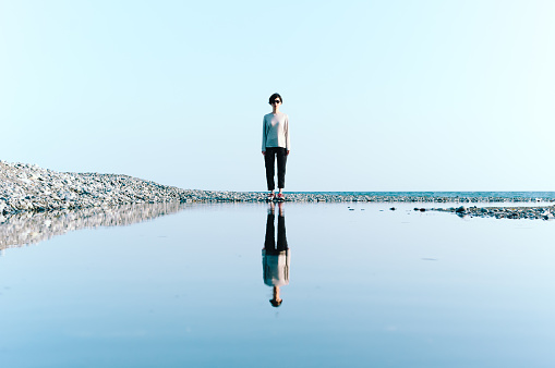 Woman Standing by Beach Reflected in Big Puddle