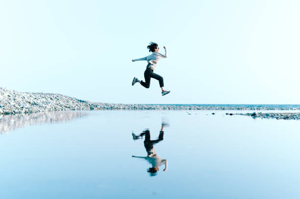 上記の大きな水たまりに映った水空中ジャンプの女性 - ジャンプする ストックフォトと画像