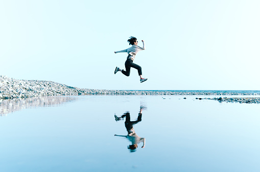 Woman in mid-air jump above water Reflected in Big Puddle