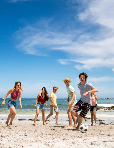 Young man playing soccer with friends at beach
