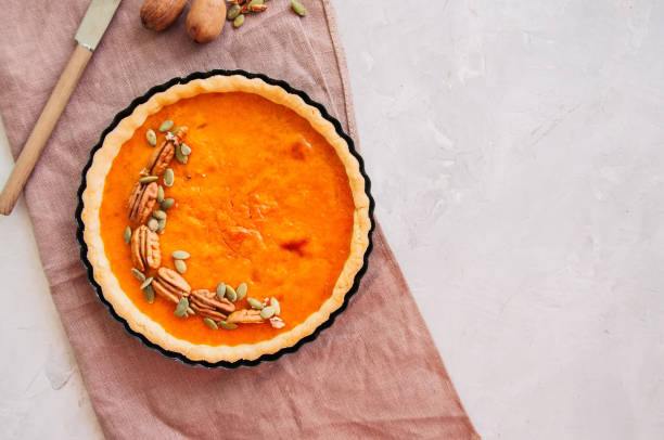 istock Traditional american baking - Pumpkin pie garnished with pecans and seeds on a white stone background 865632402