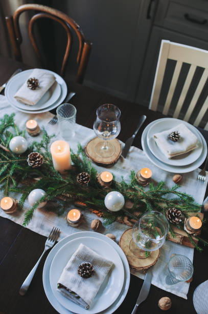 istock Festive Christmas and New Year table setting in scandinavian style with rustic handmade details in natural and white tones. Dining place decorated with pine cones, branches and candles 865640410