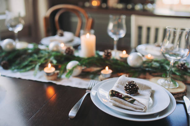 istock Festive Christmas and New Year table setting in scandinavian style with rustic handmade details in natural and white tones. Dining place decorated with pine cones, branches and candles 865640414