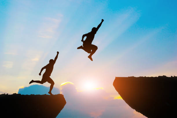 istock Men jump cliff sun light over silhouette 865647686