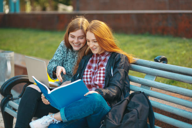istock Two students sit on bench looking in book and smiling 865665042