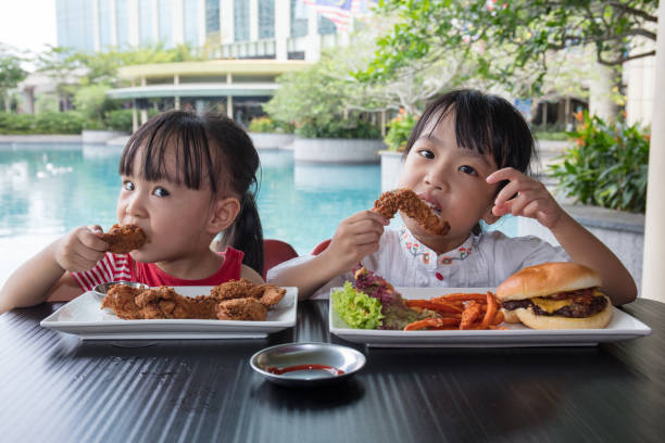 le bambine asiatiche cinesi mangiano hamburger e pollo fritto - dining burger outdoors restaurant foto e immagini stock