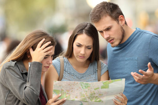 Three lost tourists trying to find a location in a map Three worried lost tourists trying to find a location in a paper map on the street lost stock pictures, royalty-free photos & images