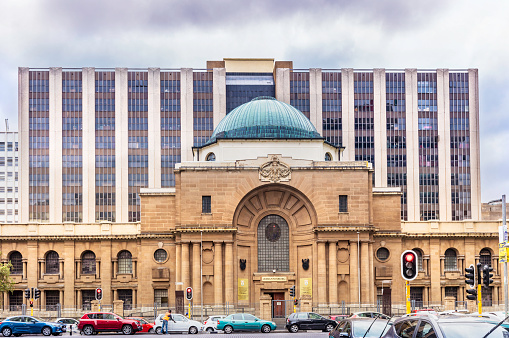 The high court building in Johannesburg city centre with trafffic and a car guard in the street.