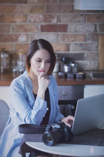 istock Beautiful young photographer sitting at kitchen with camera 865676548