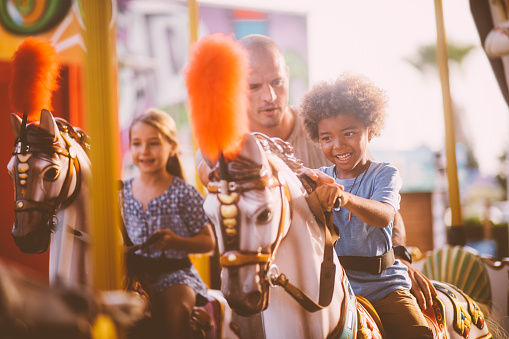 Multi-ethnic family boy having fun with father riding horse on merry-go-round amusement park ride
