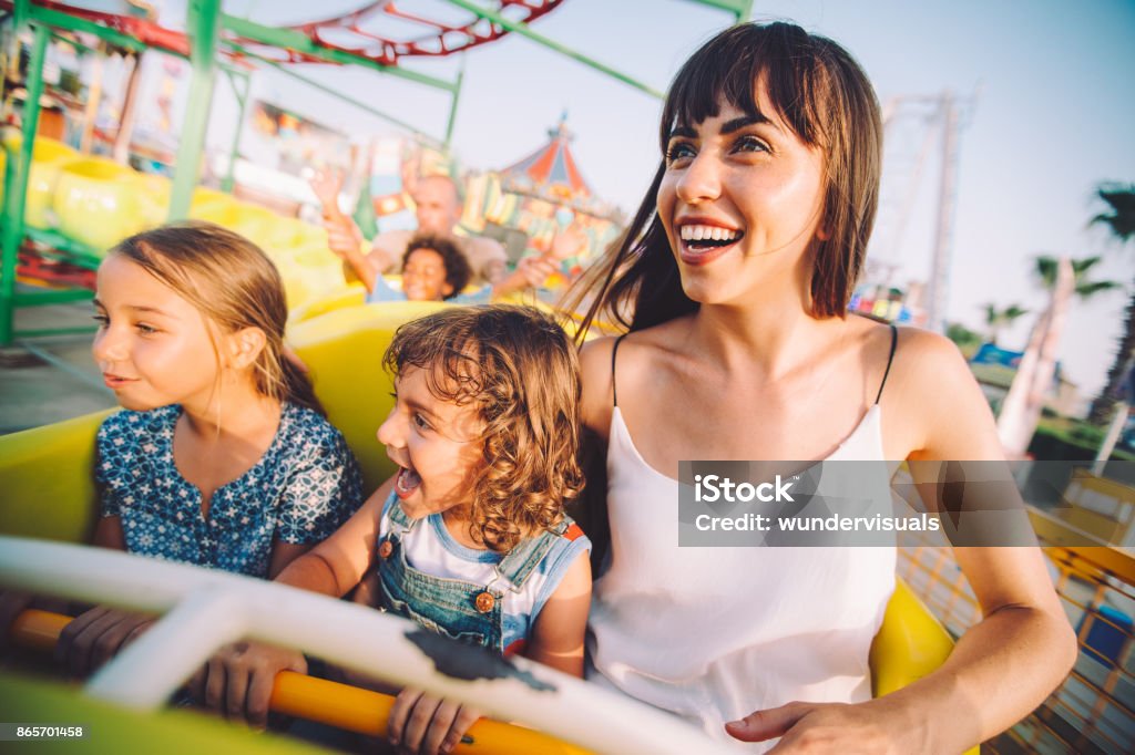 Excited son and daughter with mother on roller coaster ride Cheerful multi-ethnic children having fun with parents on roller coaster circus ride in summer Rollercoaster Stock Photo