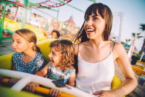 Excited son and daughter with mother on roller coaster ride Cheerful multi-ethnic children having fun with parents on roller coaster circus ride in summer rollercoaster stock pictures, royalty-free photos & images