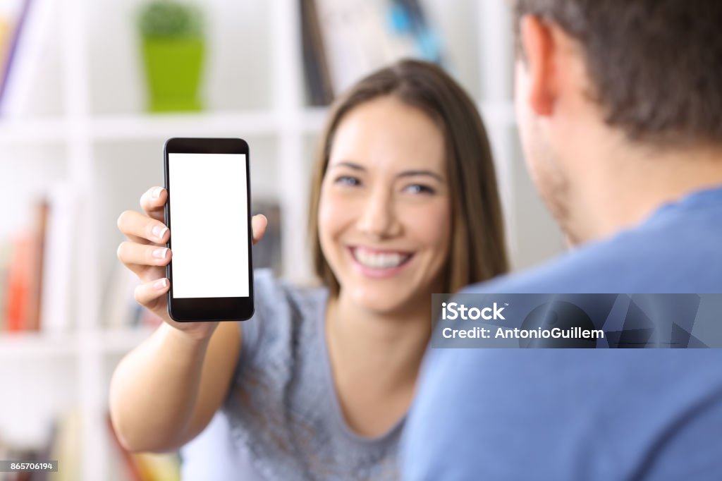 Woman showing phone screen to a friend Woman showing a smart phone screen to a friend at home Showing Stock Photo