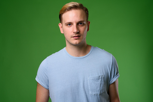 Studio shot of young handsome man with blond hair against green background