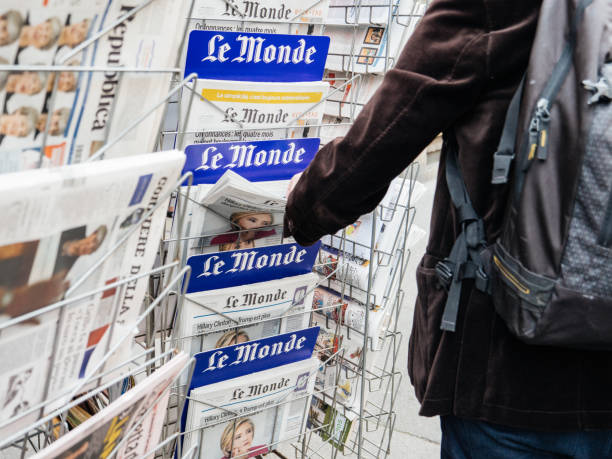 Paris: Man buying latest French Le Monde newspaper from press kiosk to read latest news scandals and journalistic investigation