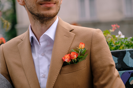Close-up man dressed in classy vintage camel jacket with three red yellow roses in pocket. Man ready for a special event, wedding, dating, fashion presentation.
