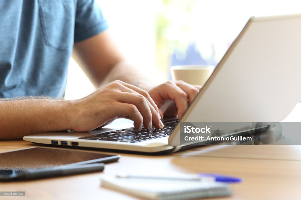 Man hands typing on a laptop keyboard on a desk Close up of man hands typing on a laptop keyboard on a desk at home or office Hand Stock Photo