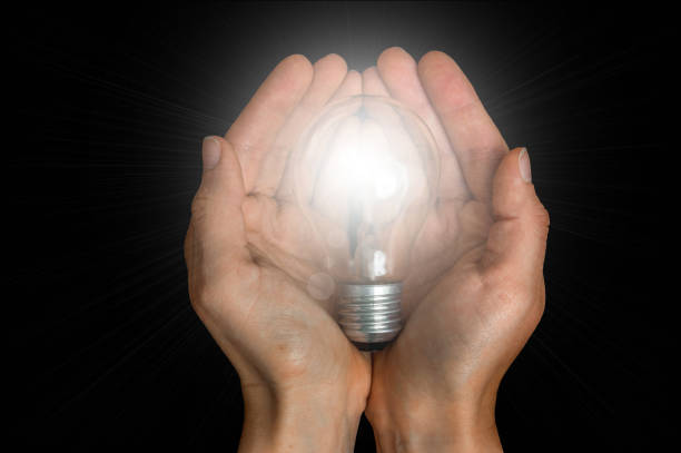 istock Glowing light bulb in female hands isolated on black 865729314