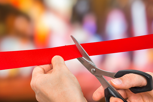 Hand with scissors cutting red ribbon - opening ceremony concept