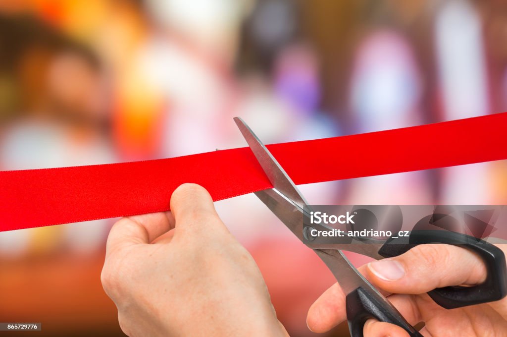 Hand with scissors cutting red ribbon - opening ceremony Hand with scissors cutting red ribbon - opening ceremony concept Ribbon Cutting Stock Photo