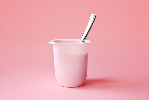 Delicious strawberry yogurt or pudding  in white plastic cup on pink background with copy space. Strawberry pink yoghurt with spoon in it. Minimal style.