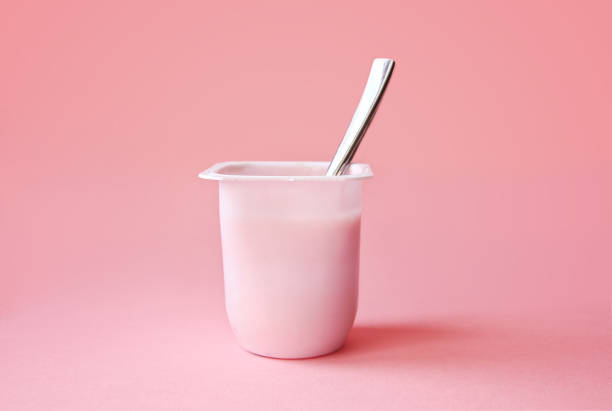 Strawberry yogurt or pudding in plastic cup on pink background Delicious strawberry yogurt or pudding in white plastic cup on pink background with copy space. Strawberry pink yoghurt with spoon in it. Minimal style. yogurt stock pictures, royalty-free photos & images