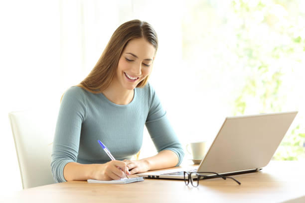 istock Woman writing notes beside a laptop at home 865741204