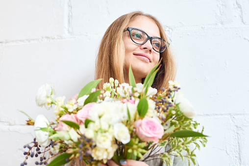 Smiling dreamy young woman in eyeglasses holding tender bouquet and looking with hope away