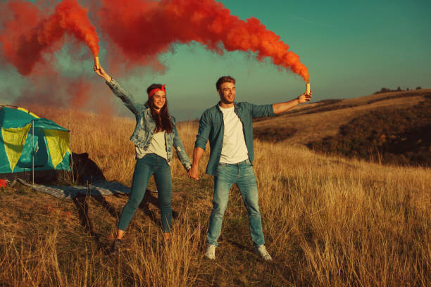 istock Young happy couple holding smoke bombs on camping 865749352
