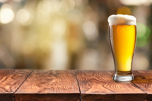glass of cold refreshing beer with foam on a wooden table with a blurred background