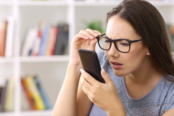 Girl with eyesight problems trying to read phone text Girl wearing eyeglasses with eyesight problems trying to read phone text at home stalker stock pictures, royalty-free photos & images